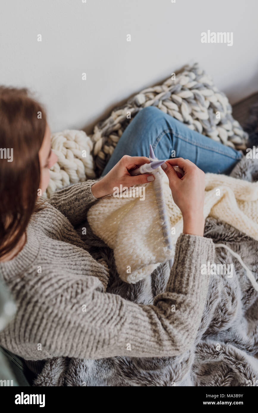 Junge Frau sitzt neben einem Kachelofen und strickt, detail, Stockfoto
