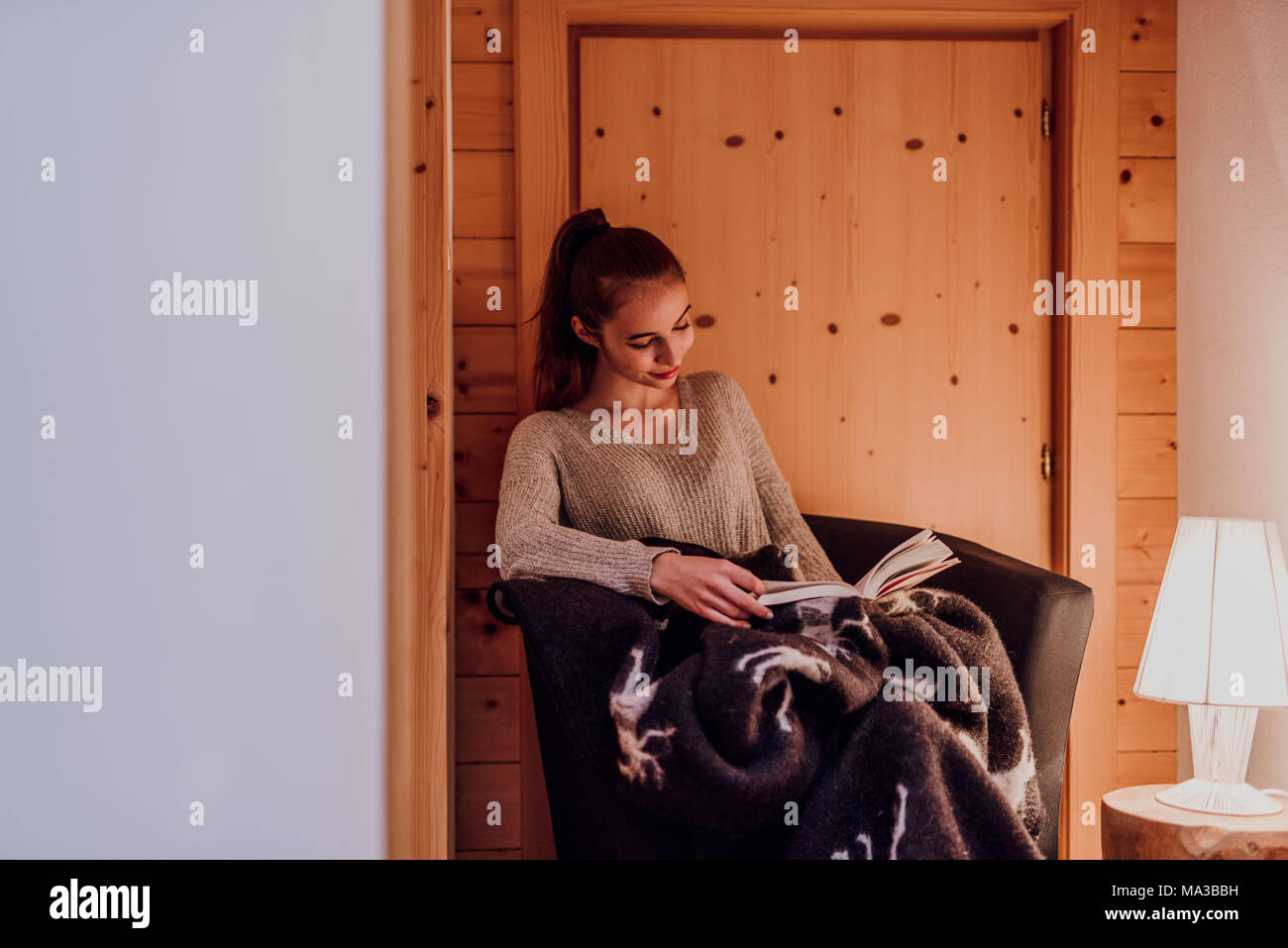 Junge Frau in eine Decke gewickelt, ein Buch lesen, Lampe, warmes Licht Stockfoto