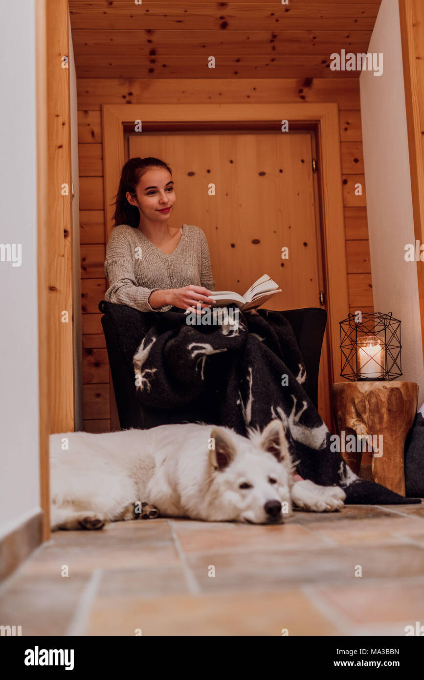 Junge Frau in eine Decke gewickelt, ein Buch lesen, Schäferhund liegt neben Ihr Stockfoto