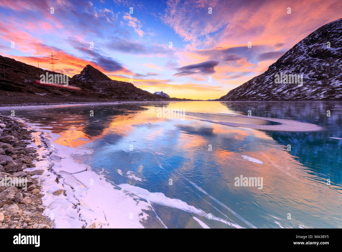 Atemberaubenden Sonnenaufgang auf dem gefrorenen Lago Bianco (Weißer See) mit Transit von Red Train., Bernina, Engadin, Graubünden, Schweiz. Stockfoto