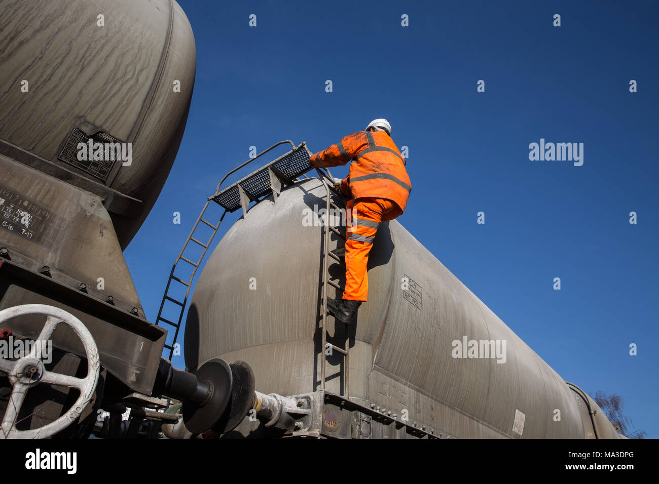 Eine Eisenbahn Wartung Arbeiter tragen Hi viz Kleidung klettern eine Leiter auf eine Profilschiene Tanker das obere Deck während Arbeiten in großer Höhe zu prüfen. Stockfoto