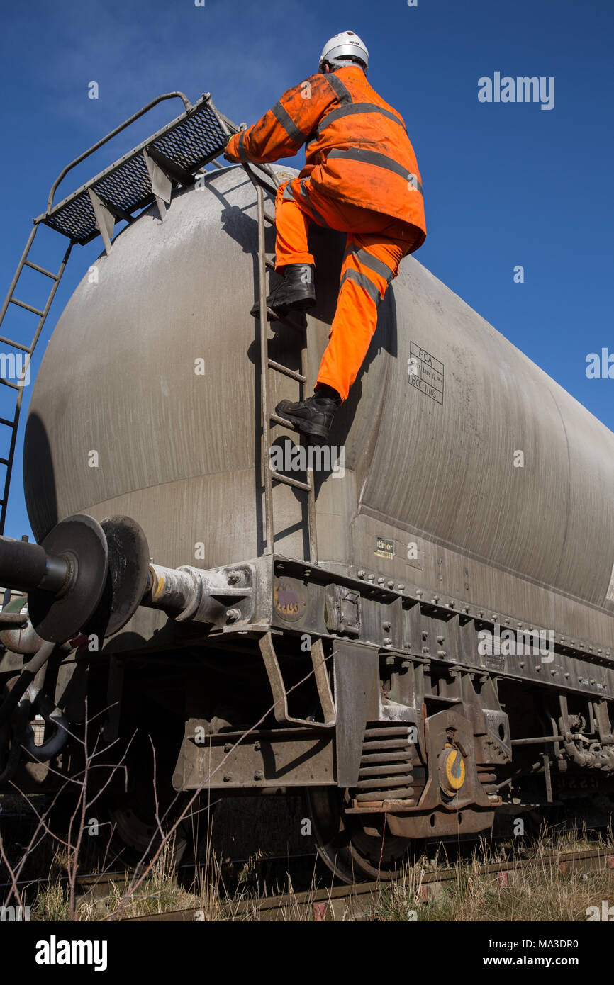 Eine Eisenbahn Wartung Arbeiter tragen Hi viz Kleidung klettern eine Leiter auf eine Profilschiene Tanker das obere Deck während Arbeiten in großer Höhe zu prüfen. Stockfoto