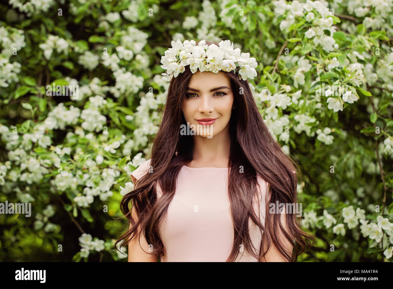 Junge lächelnde Frau mit Blumen Kranz. Nettes Mädchen mit Make-up, Blumen und lange glatte Haare auf floral background im Freien Stockfoto