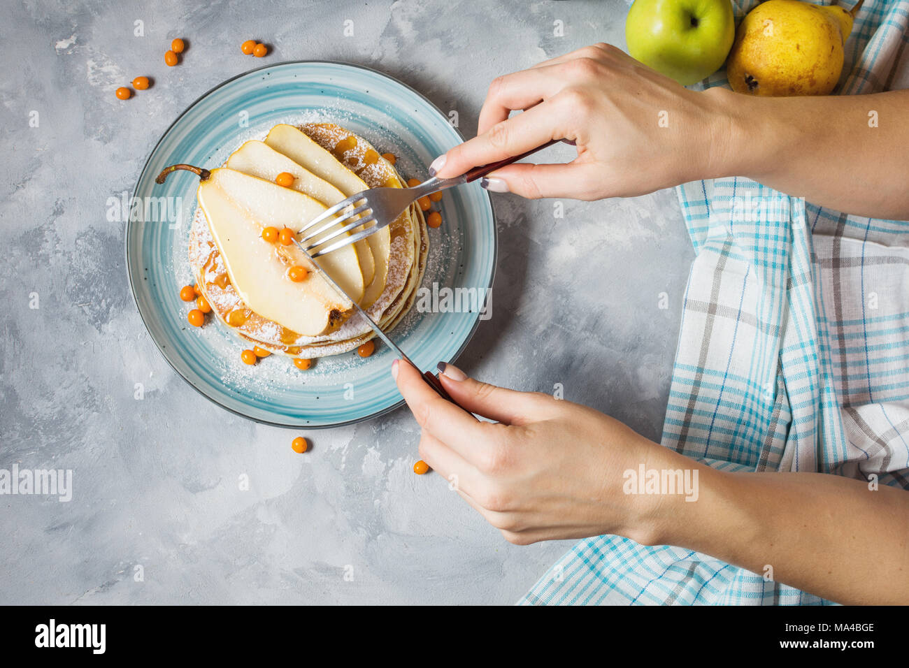 Hausgemachte Frühstück: amerikanische Pfannkuchen serviert mit Beeren, Birnen und Honig auf konkreten Hintergrund. Frau Hände, Pfannkuchen, Ansicht von oben Stockfoto