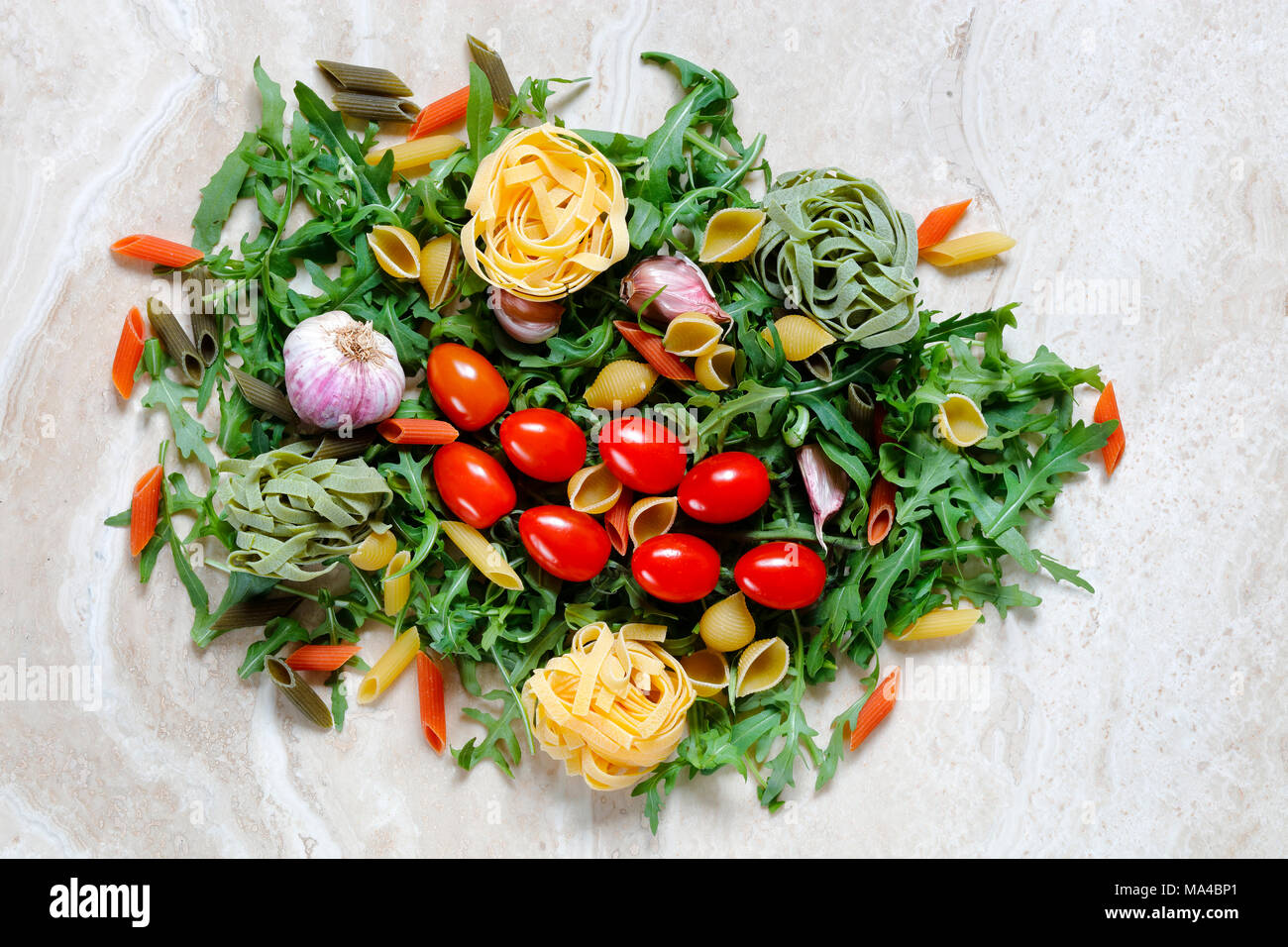 Rucola Rucola mit Pflaumen Tomaten und Knoblauch mit Tagliatelle und Penne Pasta tricolore Zutaten für italienische Küche auf Marmor tisch Stockfoto