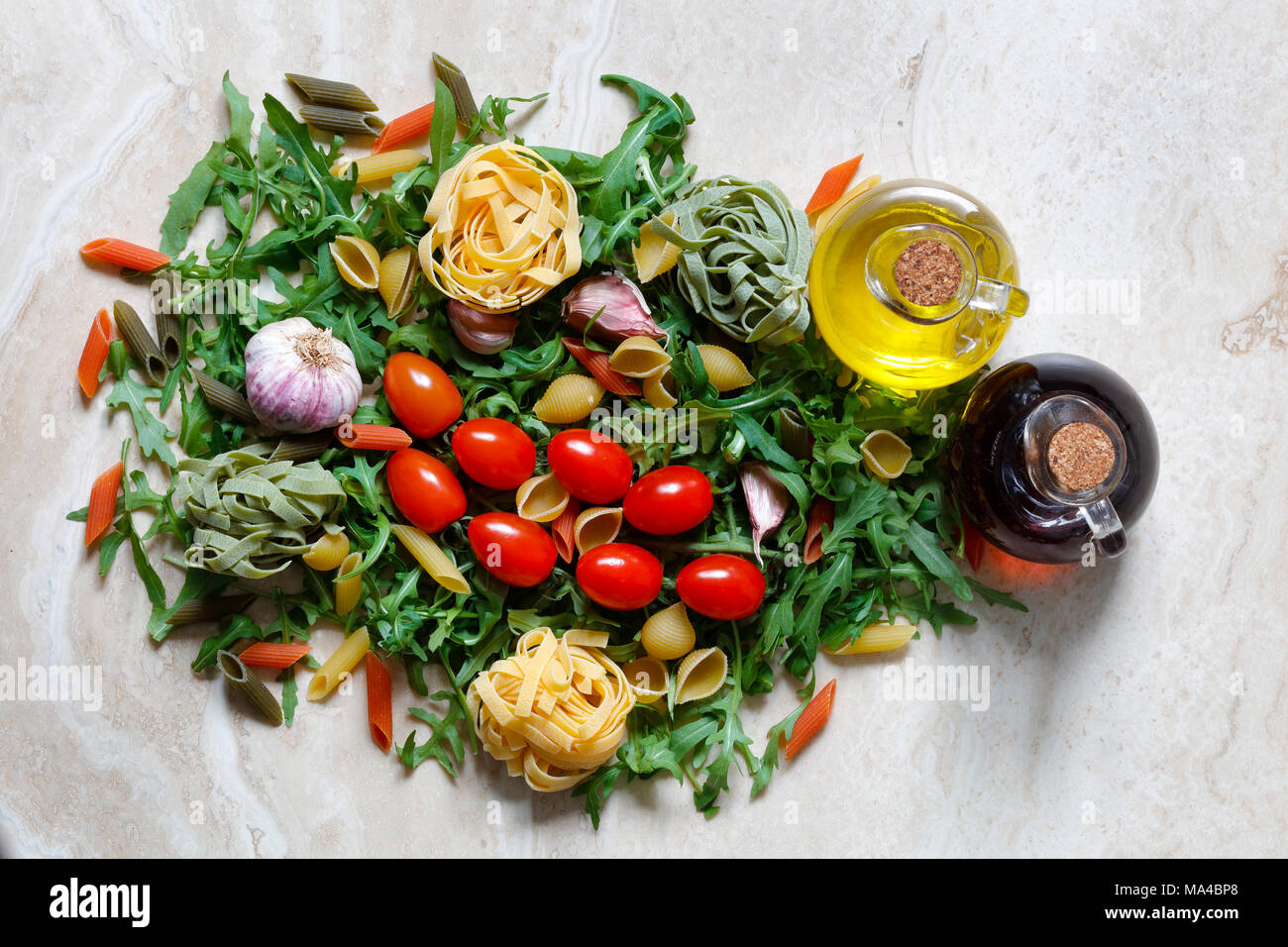 Rucola Rucola mit Pflaumen Tomaten und Knoblauch mit Tagliatelle und Penne Pasta tricolore Zutaten für italienische Küche auf Marmor tisch mit Olivenöl Stockfoto