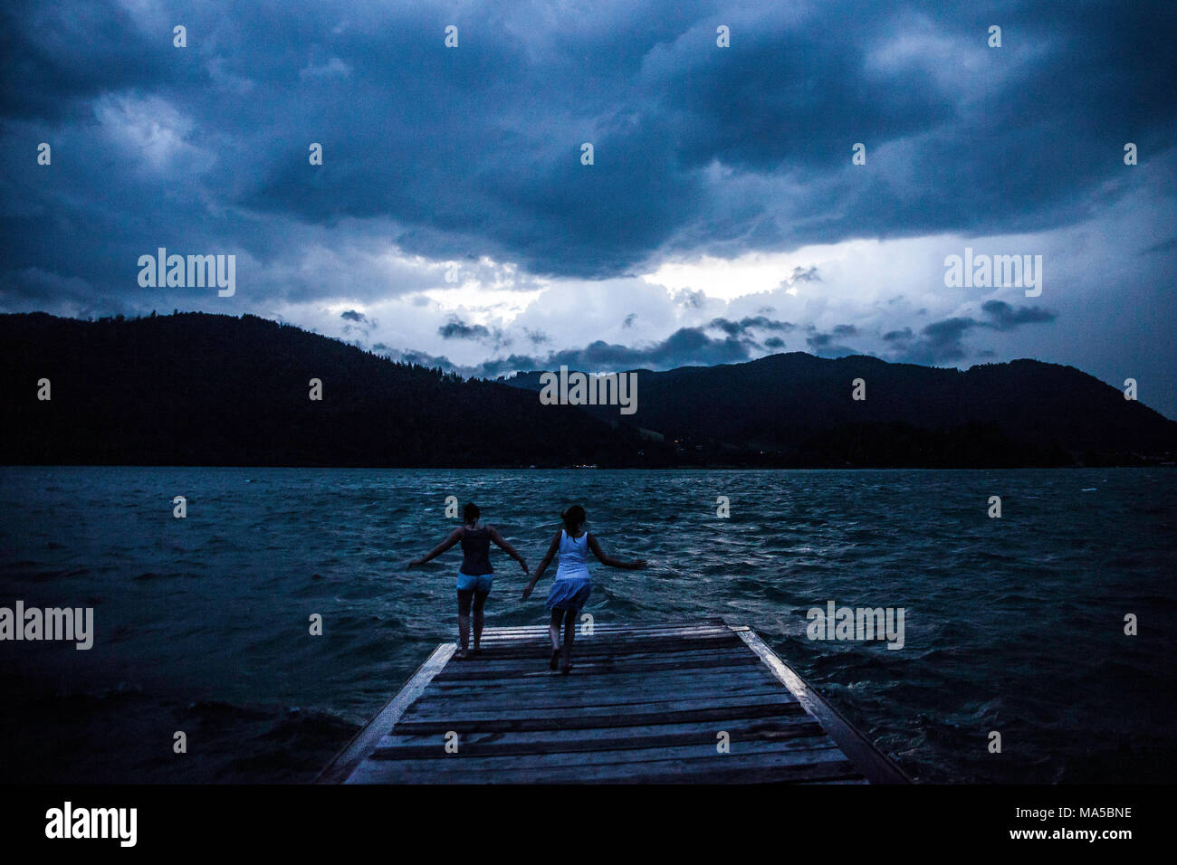 Zwei Mädchen springen auf einem Steg am Schliersee (See) in Erwartung der ein schweres Gewitter Stockfoto