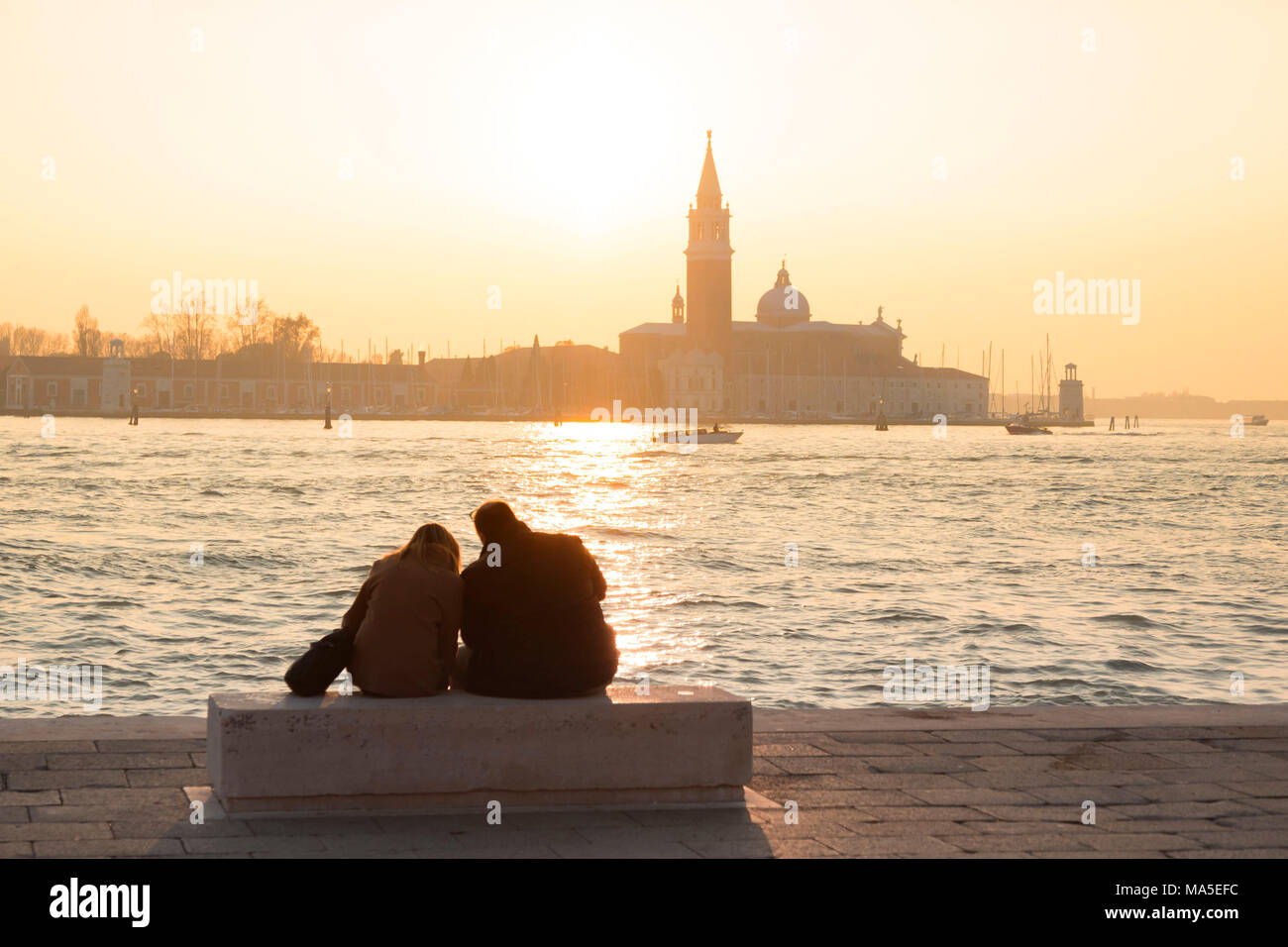 Paar Touristen bewundern Sie den Sonnenuntergang in Richtung der Insel San Giorgio Maggiore von den Ufern des Canal Grande, Venedig, Venetien, Italien Stockfoto
