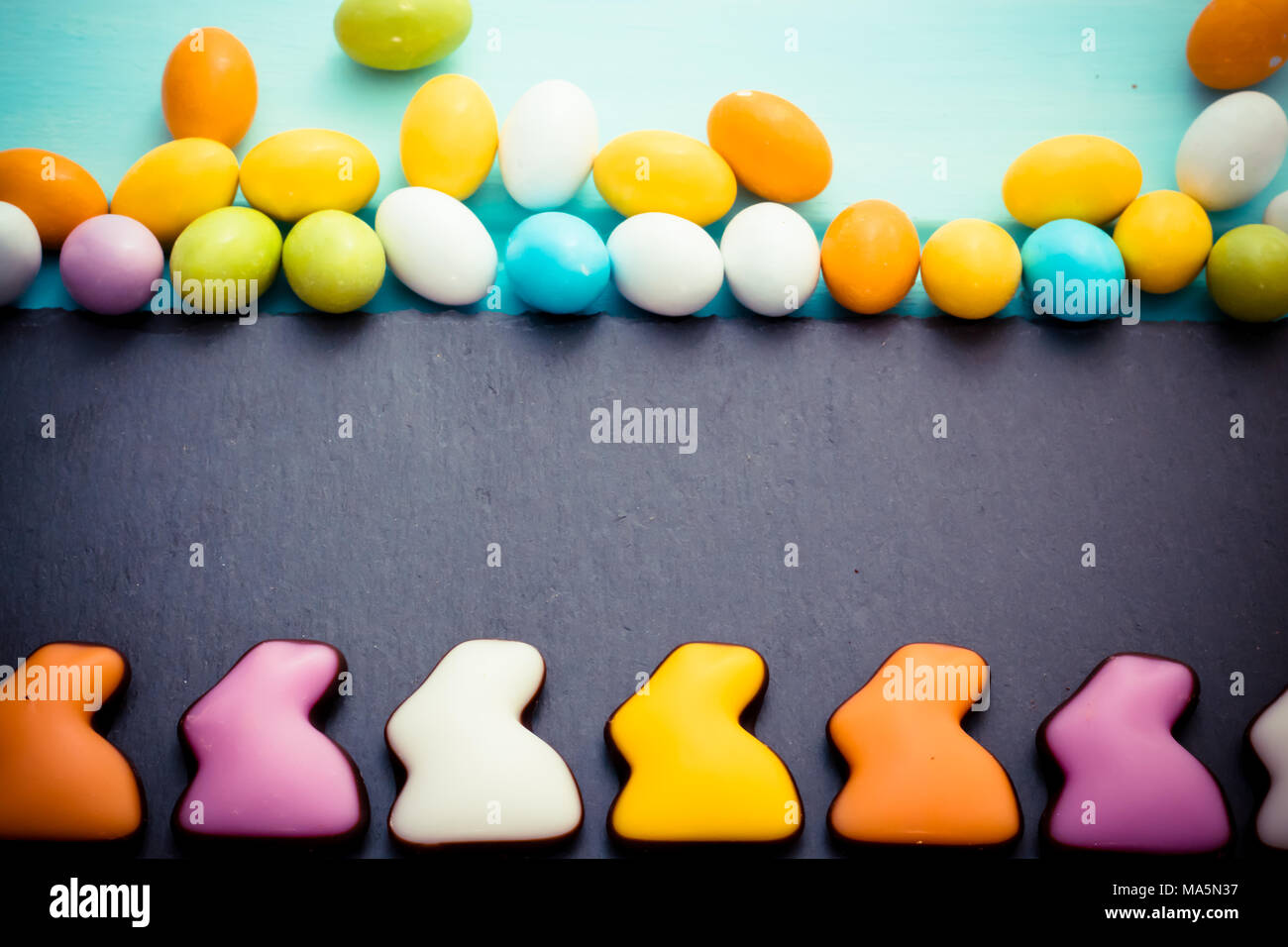Frohe Ostern. Bunte Schokolade Kaninchen in einer Reihe mit kleinen Pastell süße Eier auf schiefer Schneidebrett schwarz blau Hintergrund. Ansicht von oben. Copyspace Stockfoto