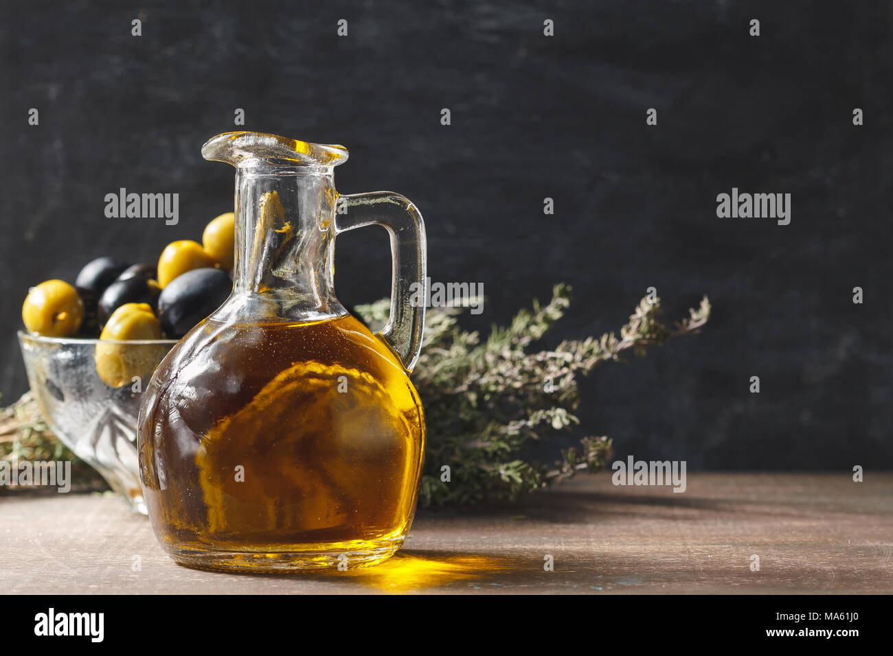 Glas Flasche premium natives Olivenöl, Schüssel mit Oliven und Kräutern auf dunklem Hintergrund, rustikalen Stil Stockfoto