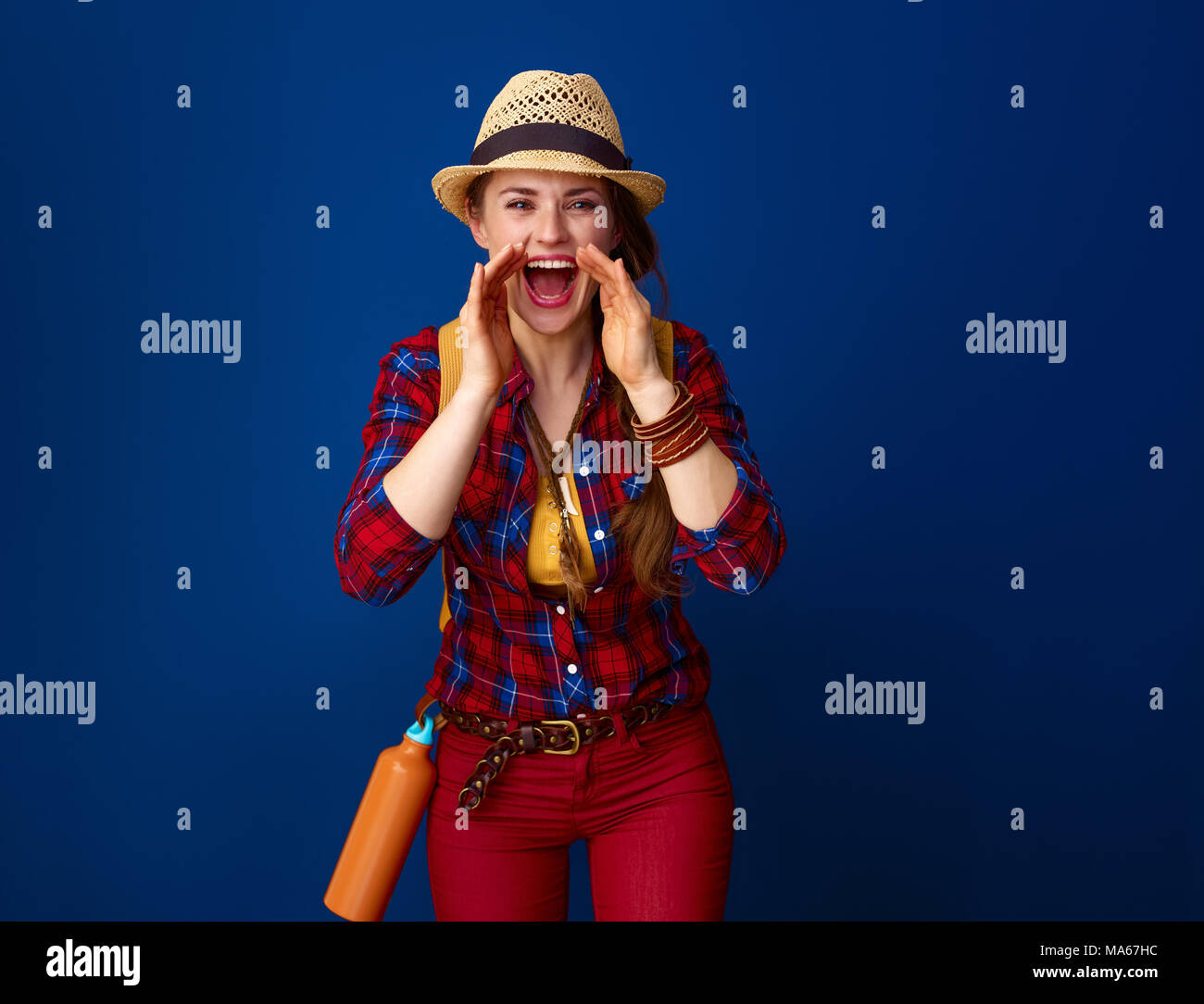 Auf der Suche nach inspirierenden Orten. lächelnden jungen Frau Wanderer in einen Plaid Shirt Schreien über Megaphon geformten Hände isoliert auf Blau Stockfoto