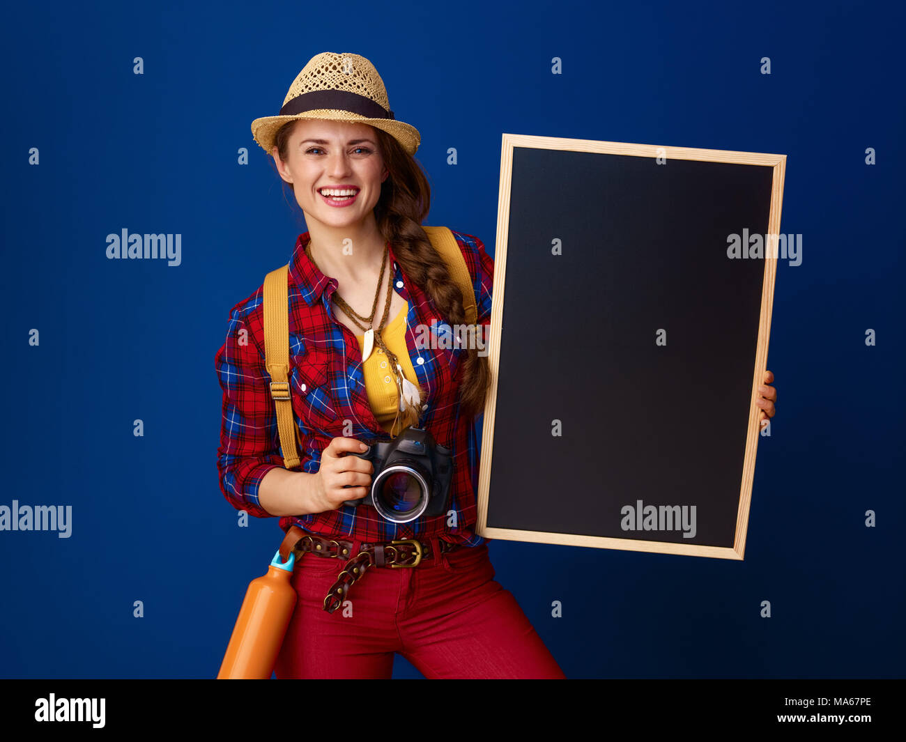 Auf der Suche nach inspirierenden Orten. glückliche junge Frau Wanderer mit Rucksack und Digitalkamera übersicht Tafel vor blauem Hintergrund Stockfoto