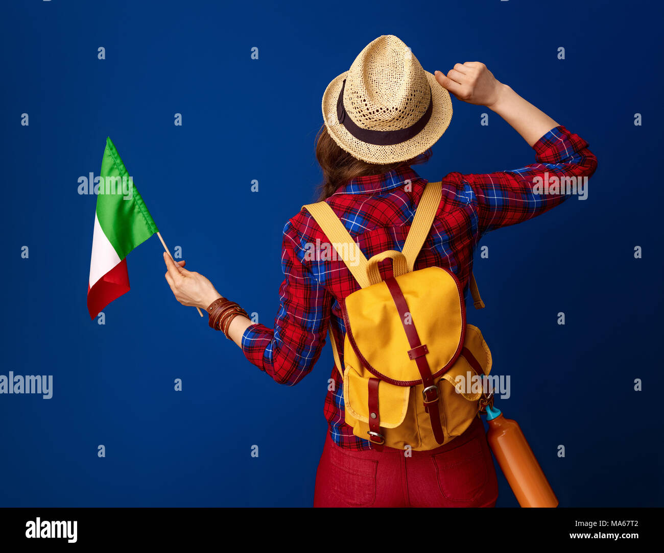 Auf der Suche nach inspirierenden Orten. Hinter der jungen Frau Wanderer mit Rucksack und die Flagge von Italien gesehen isoliert auf Blau Stockfoto