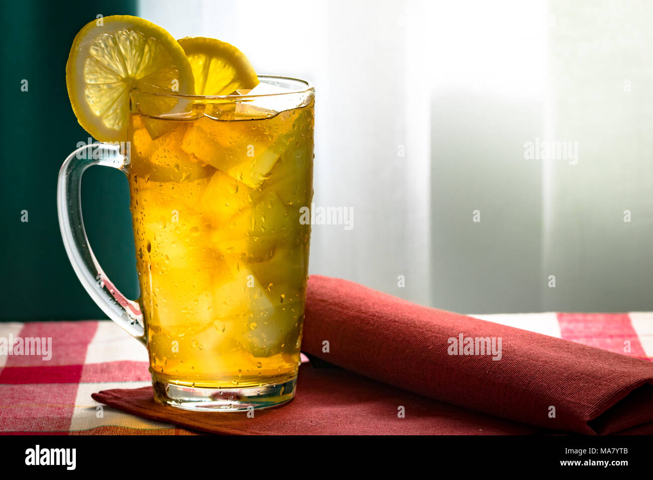 Kalter Tee mit Zitrone und Eiswürfel in ein hohes Glas Schale transparent rot Serviette Stockfoto
