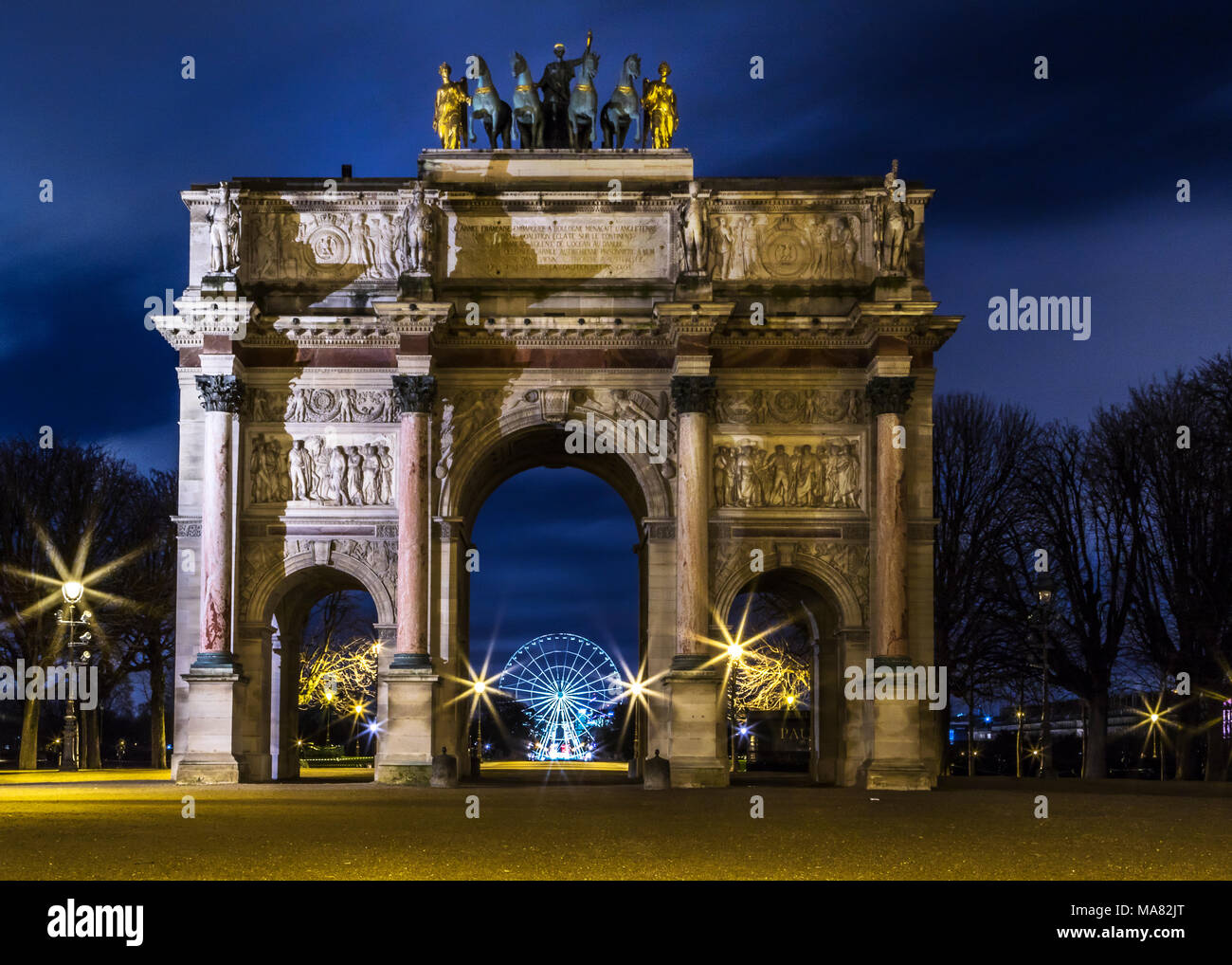 Arc de Triomphe du Carrousel nachts Framing der Roue de Paris Rad über die zentrale Arch, durch Baum Silhouetten und funkelnde Lampen flankiert Stockfoto