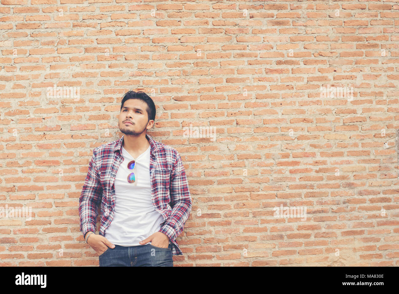 Jungen gutaussehenden Mann, der Coolness Plaid Shirt und Jeans gegen eine Mauer. Stockfoto