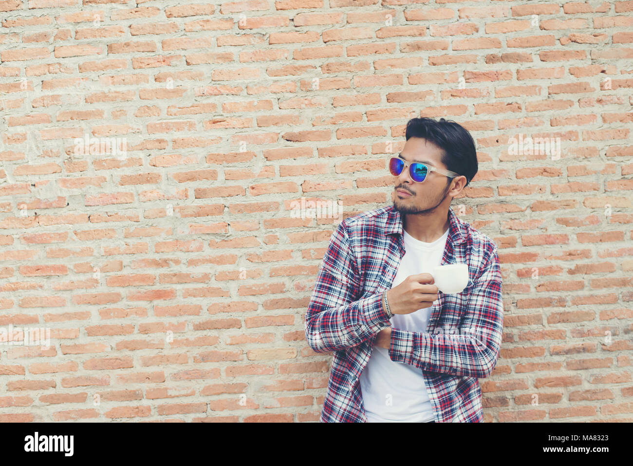 Stattliche hipster jungen Mann mit Kaffeetasse und weg schauen, während auf der Straße gegen die Mauer im Hintergrund stehen. Stockfoto