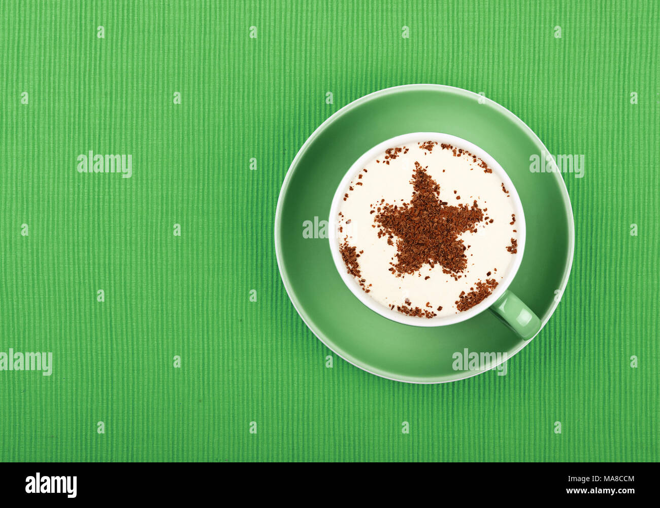 Nahaufnahme einer Latte Cappuccino mit sternförmigen Schokolade Milch topping in rot Tasse mit Untertasse über Hintergrund grün Tischdecke, erhöhte Top Stockfoto