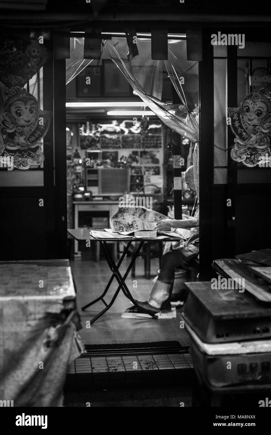 Ein Mann sitzt an seinem Tisch im Gehäuse der Märkte von Tai O, Hong Kong Stockfoto