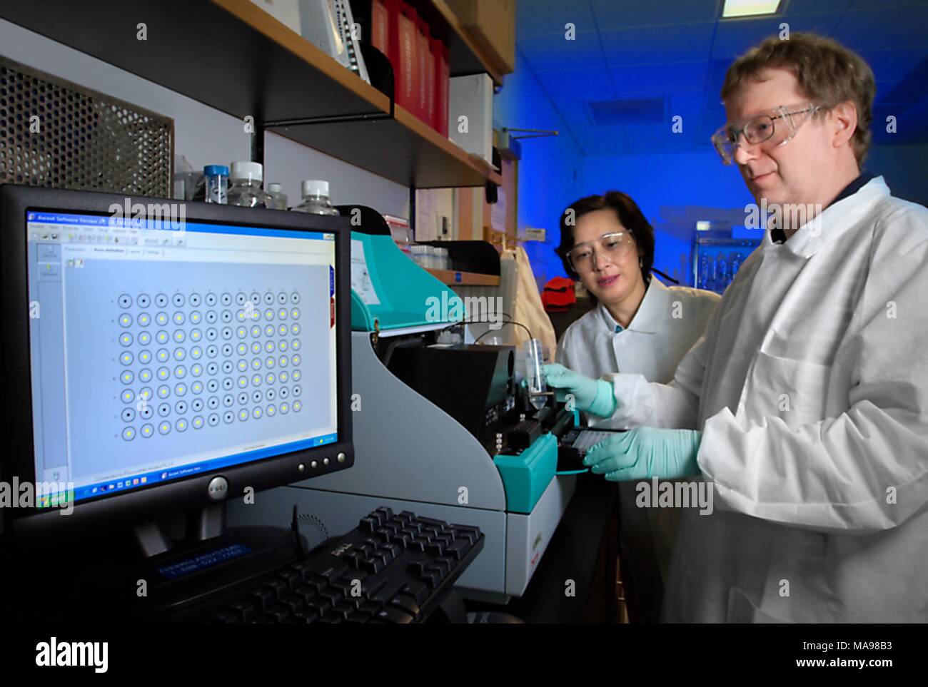 Foto von Dr. Davis Lupo, ein Biologe an der CDC arbeiten, und Lee Lam, beide NCHHTSP Mitarbeiter, Arbeiten in einem Labor mit Schutzkleidung neben Maschinen, mit einem luminometer HIV-Infektion von menschlichen Zellen in vitro, 2007 zu messen. Mit freundlicher CDC/Hsi Liu, James Gathany. () Stockfoto