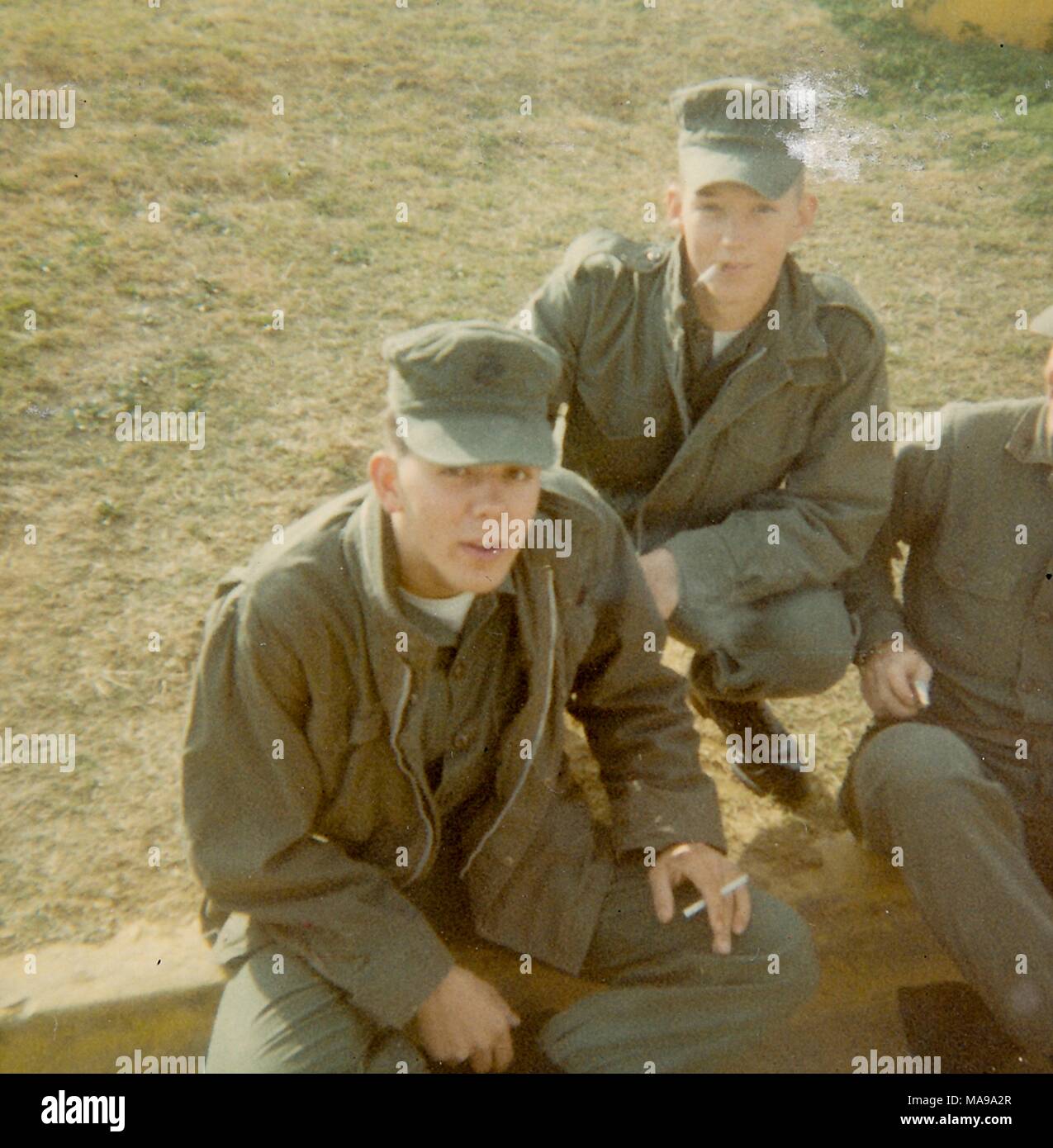 Farbfoto, geschossen von einem hohen Winkel, von zwei Soldaten das Tragen von Uniformen und Hüte, und Zigaretten zu rauchen, während auf dem Bordstein sitzen neben eine Rasenfläche, die in Vietnam während des Vietnam Krieges, 1968 fotografiert. () Stockfoto