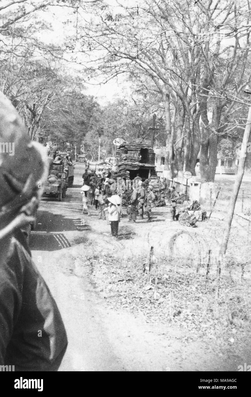 Schwarz-weiß Foto, zeigt sowohl die uniformierte Soldaten und vietnamesische Volk in ziviler Kleidung, Stehen, Gehen und Reiten in Lastwagen, vorbei an einem sandsack Bunker, in einem Gebiet mit vielen Bäumen, die in Vietnam während des Vietnam Krieges fotografiert (1955-1975), 1971. () Stockfoto