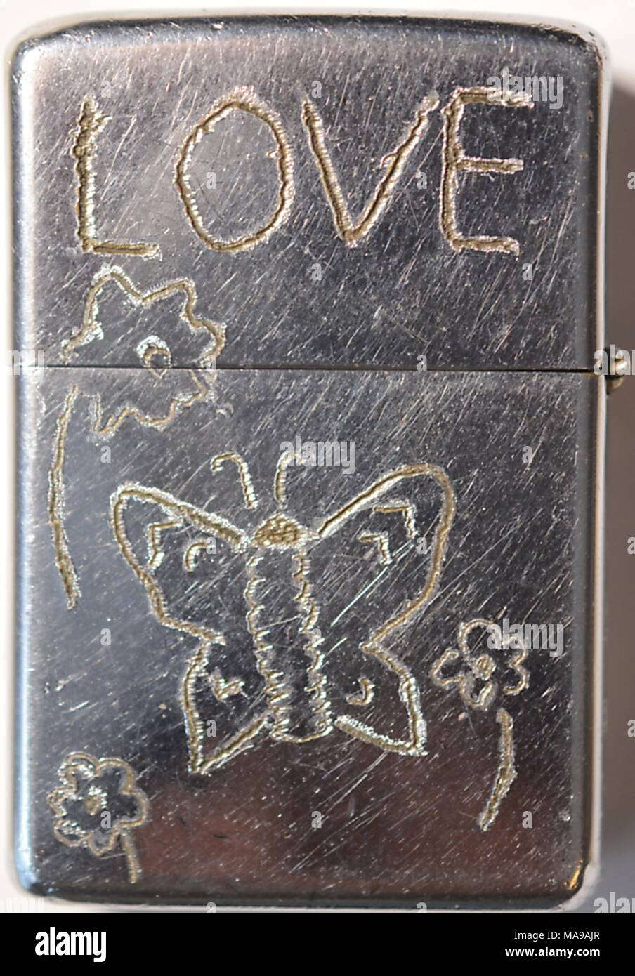 In der Nähe von Metall Zippo Feuerzeug, auf dem der Besitzer der Hand hat - gravierte hippie Symbolik, die das Wort Liebe und ein Schmetterling und Blumen Motiv, während des Vietnamkriegs, 1968. () Stockfoto