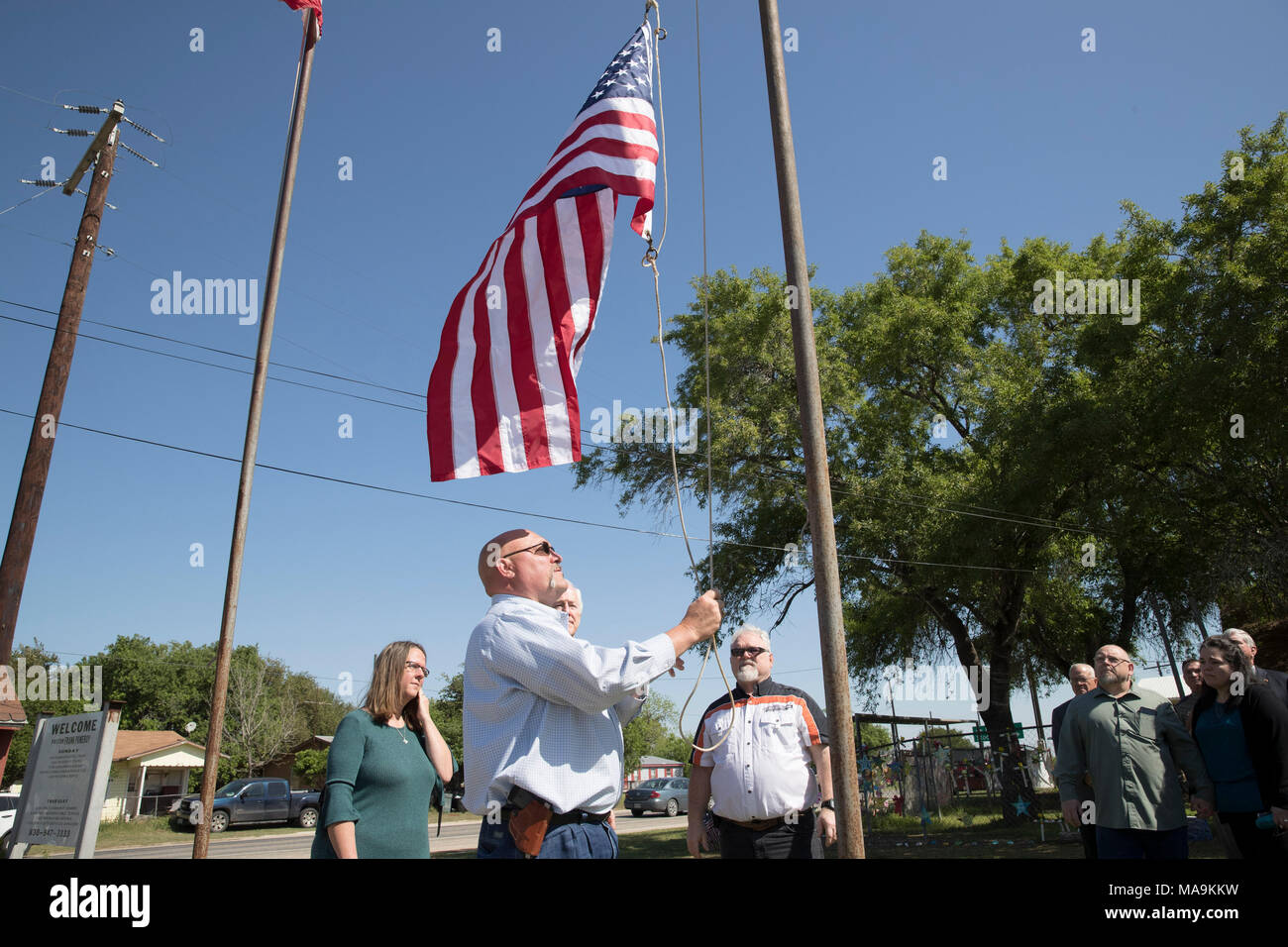 Pastor Frank Pomeroy wirft eine amerikanische Flagge auf der Website von einem Shooting, 26 leben außerhalb der First Baptist Church von Sutherland Springs während einer Presseveranstaltung fünf Monate nach dem Massaker behauptete. Us-Senator John Cornyn steht auf der rechten Seite. Stockfoto