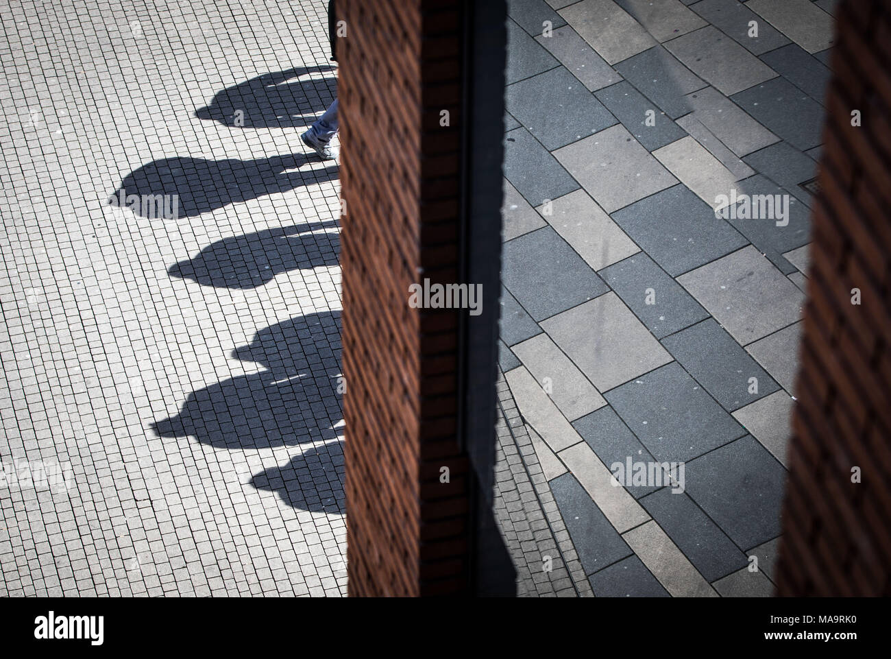 31 März 2018, Deutschland, Wiesbaden: Die mittagssonne Casting Shadows (L) von einer Gruppe von Bauarbeitern auf dem Beton vor einem Einkaufszentrum in der Innenstadt von Wiesbaden. Ein weiterer Teil der Plaza des Einkaufszentrums wird durch die Glasscheibe auf der rechten wider. Foto: Frank Rumpenhorst/dpa Stockfoto