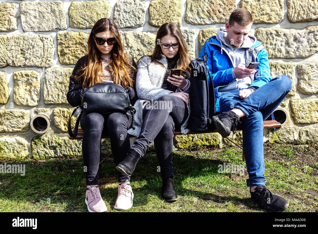 Junge drei Teenager Mobiltelefone SMS Suchen zwei Girs ein Mann mit Smartphones Teenager-Telefon sitzt auf Bank Junge Leute Generation Jugend Stockfoto