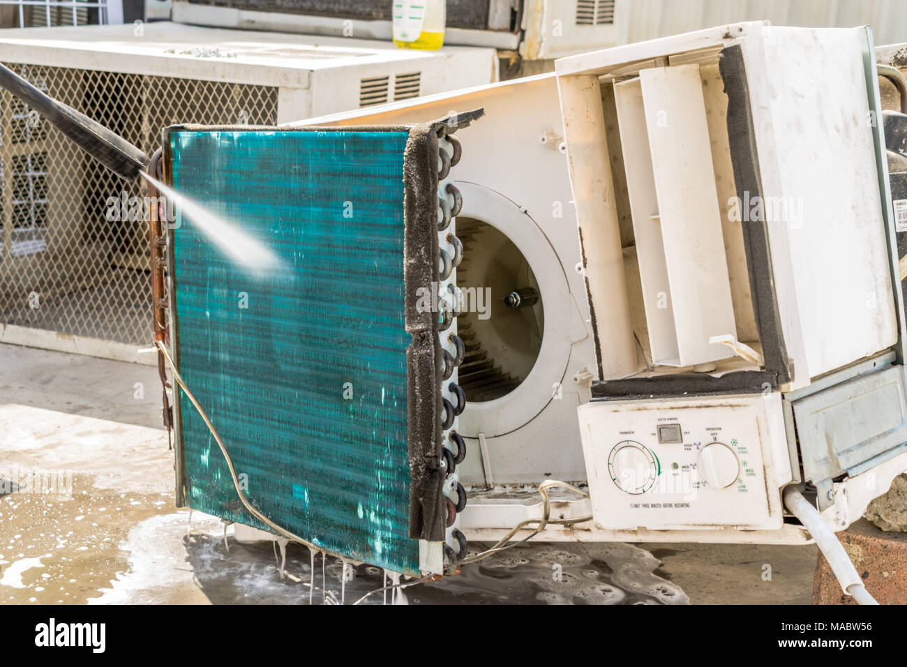 Einen professionellen Elektriker ist die Reinigung der Fenster Klimaanlage auf dem Dach eines Hauses mit seinem hohen Druck Wasser Pistole und trägt blaue Shorts Stockfoto