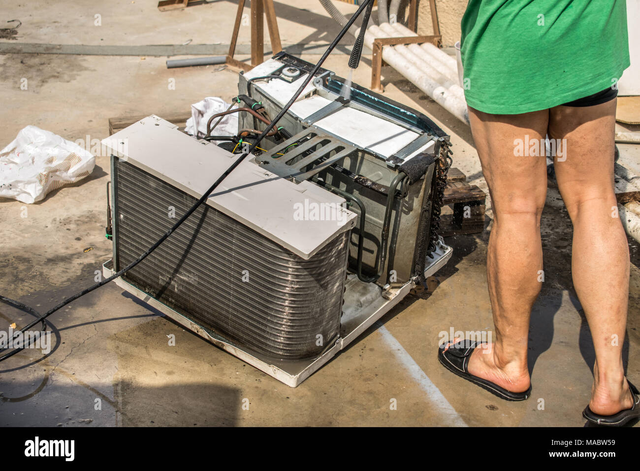 Einen professionellen Elektriker ist die Reinigung der Fenster Klimaanlage auf dem Dach eines Hauses mit seinem hohen Druck Wasser Pistole und trägt blaue Shorts Stockfoto