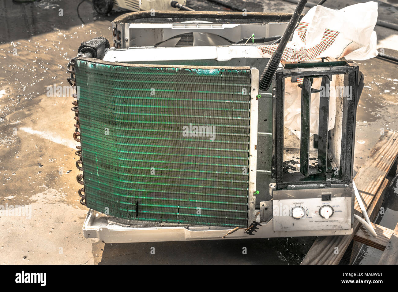 Einen professionellen Elektriker ist die Reinigung der Fenster Klimaanlage auf dem Dach eines Hauses mit seinem hohen Druck Wasser Pistole und trägt blaue Shorts Stockfoto