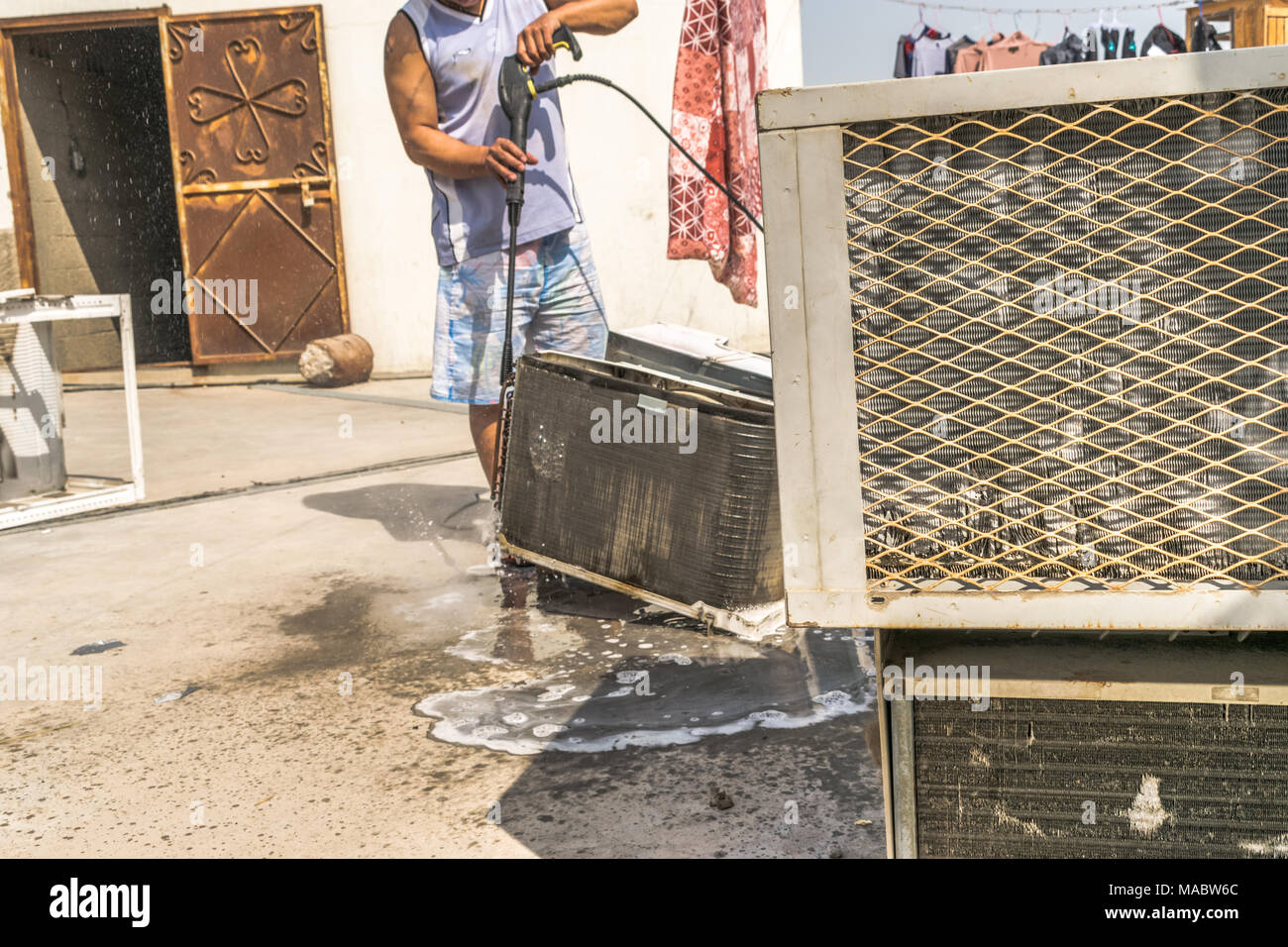 Einen professionellen Elektriker ist die Reinigung der Fenster Klimaanlage auf dem Dach eines Hauses mit seinem hohen Druck Wasser Pistole und trägt blaue Shorts Stockfoto