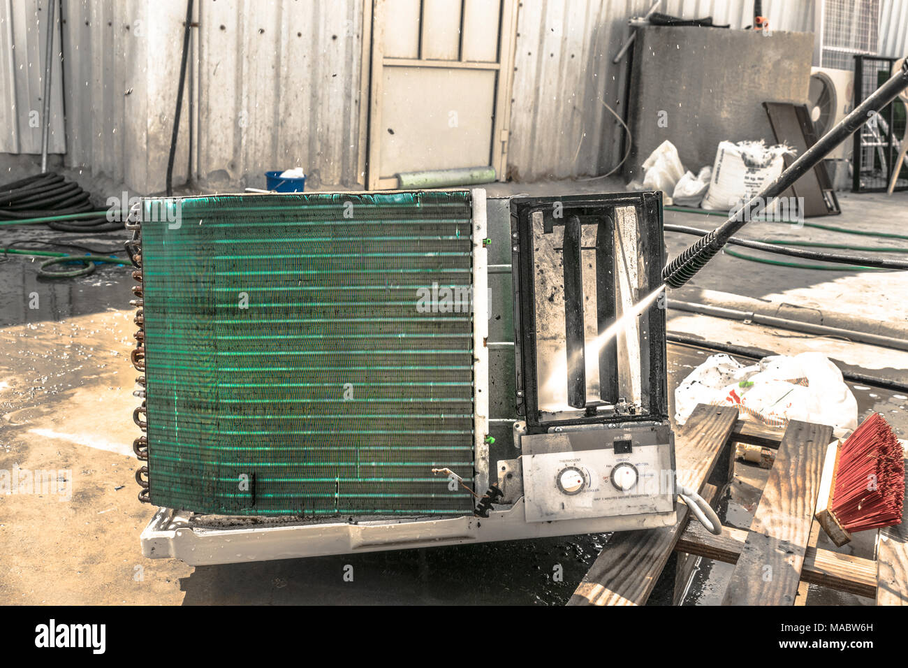 Einen professionellen Elektriker ist die Reinigung der Fenster Klimaanlage auf dem Dach eines Hauses mit seinem hohen Druck Wasser Pistole und trägt blaue Shorts Stockfoto