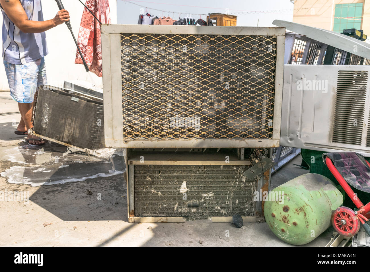 Einen professionellen Elektriker ist die Reinigung der Fenster Klimaanlage auf dem Dach eines Hauses mit seinem hohen Druck Wasser Pistole und trägt blaue Shorts Stockfoto