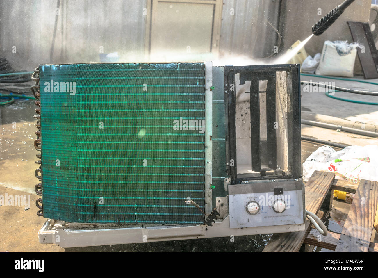 Einen professionellen Elektriker ist die Reinigung der Fenster Klimaanlage auf dem Dach eines Hauses mit seinem hohen Druck Wasser Pistole und trägt blaue Shorts Stockfoto