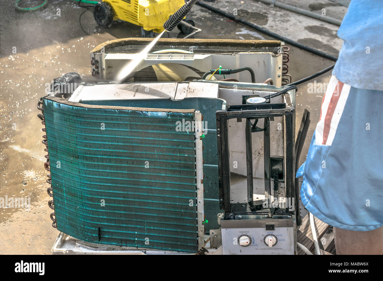 Einen professionellen Elektriker ist die Reinigung der Fenster Klimaanlage auf dem Dach eines Hauses mit seinem hohen Druck Wasser Pistole und trägt blaue Shorts Stockfoto