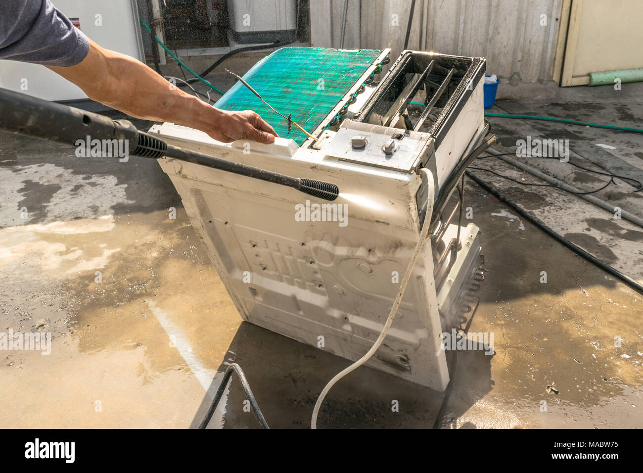 Einen professionellen Elektriker ist die Reinigung der Fenster Klimaanlage auf dem Dach eines Hauses mit seinem hohen Druck Wasser Pistole und trägt blaue Shorts Stockfoto