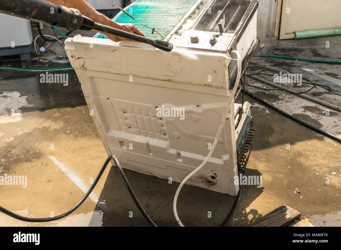 Einen professionellen Elektriker ist die Reinigung der Fenster Klimaanlage auf dem Dach eines Hauses mit seinem hohen Druck Wasser Pistole und trägt blaue Shorts Stockfoto