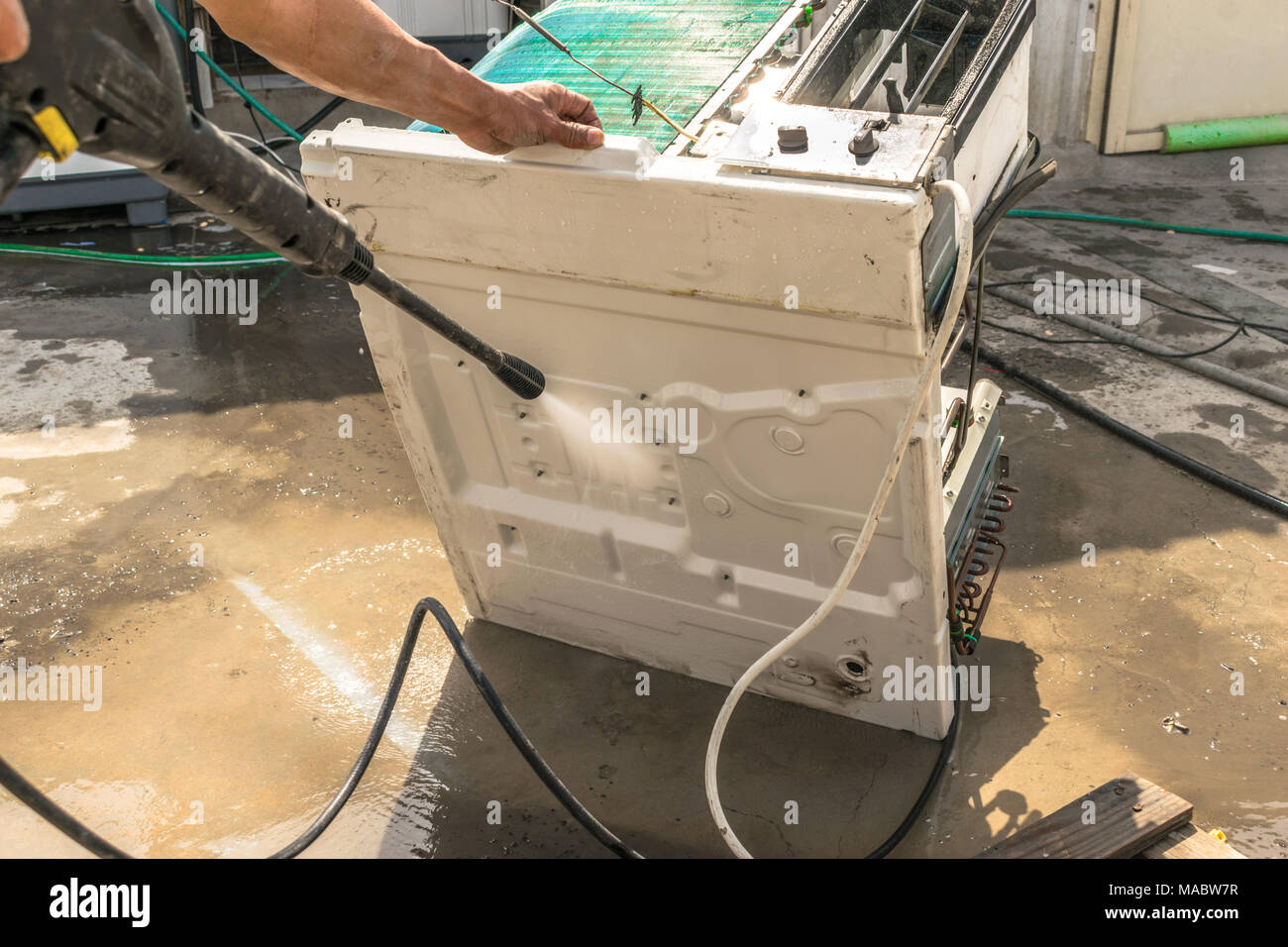 Einen professionellen Elektriker ist die Reinigung der Fenster Klimaanlage auf dem Dach eines Hauses mit seinem hohen Druck Wasser Pistole und trägt blaue Shorts Stockfoto