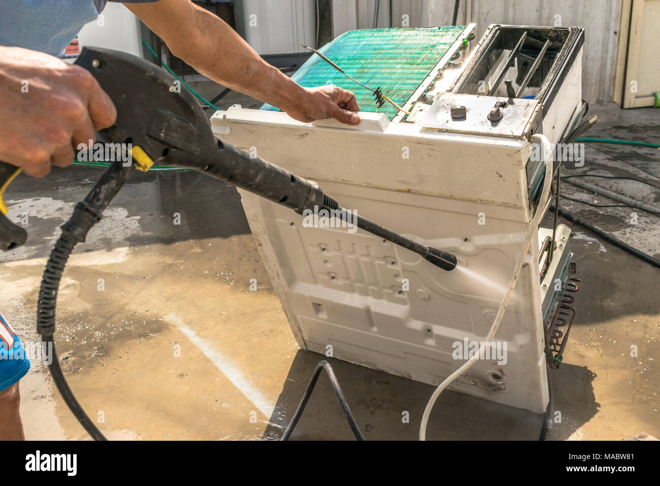 Einen professionellen Elektriker ist die Reinigung der Fenster Klimaanlage auf dem Dach eines Hauses mit seinem hohen Druck Wasser Pistole und trägt blaue Shorts Stockfoto