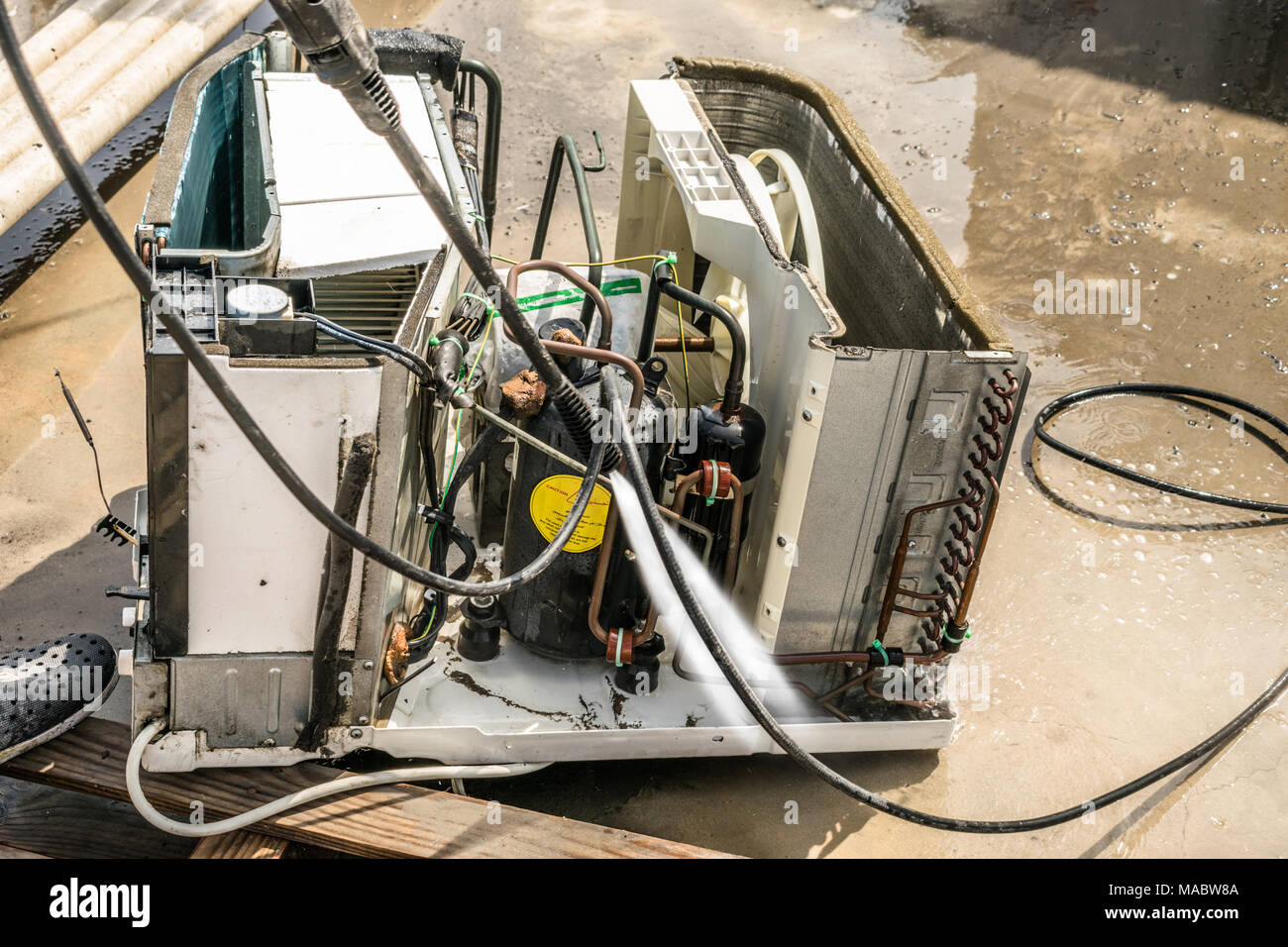 Einen professionellen Elektriker ist die Reinigung der Fenster Klimaanlage auf dem Dach eines Hauses mit seinem hohen Druck Wasser Pistole und trägt blaue Shorts Stockfoto