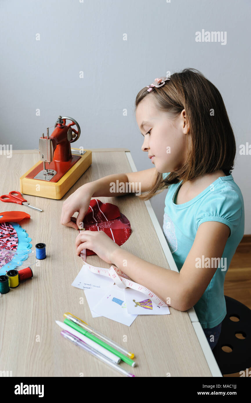 Das Mädchen ist das Nähen eines Kleides für eine Puppe. Sie mit einem Maßband, das Produkt zu messen. Stockfoto