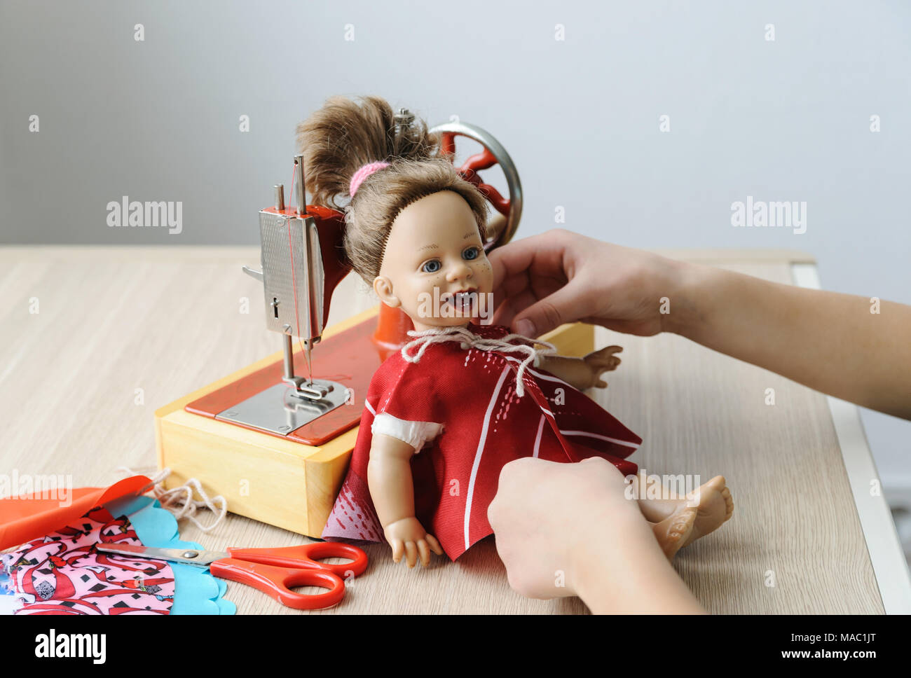 Ein Mädchen hat ein neues Kleid genäht und richtete es auf eine Puppe. Stockfoto