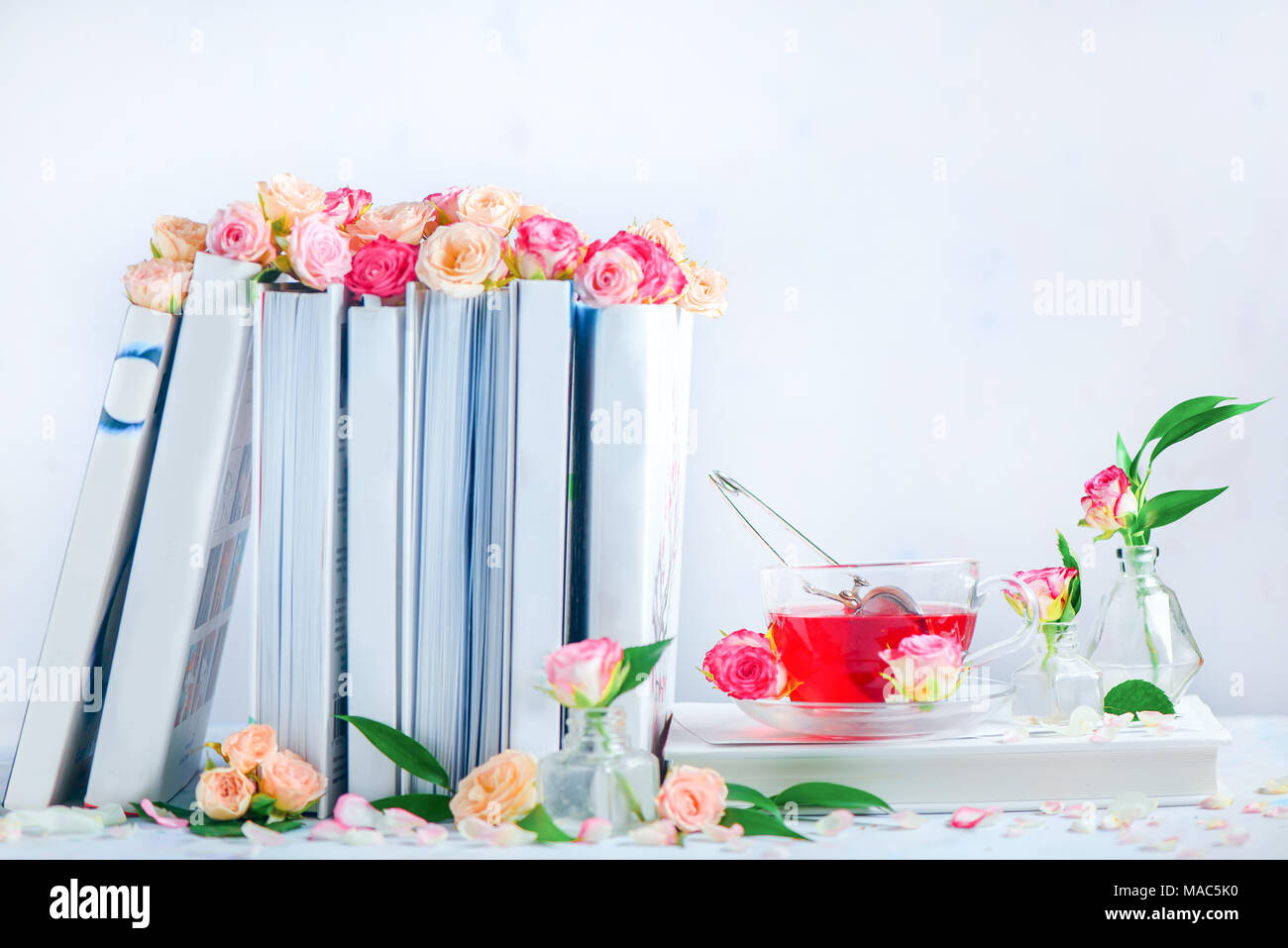Bücherregal mit weißen Bücher, Rosen und einer Tasse Kräutertee. Romantische Stillleben mit kopieren. Feder Freizeitaktivitäten und lesen Konzept. Stockfoto