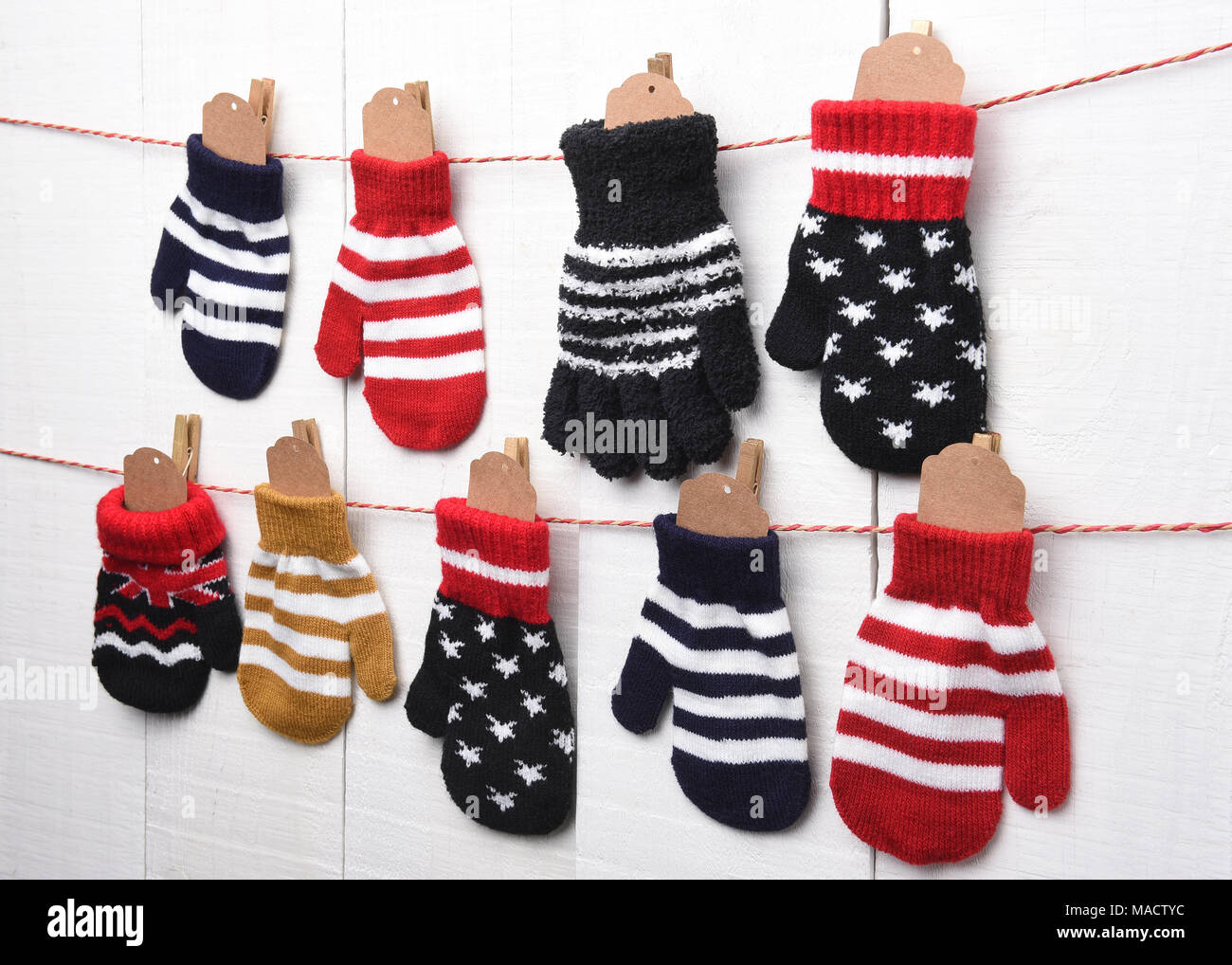 Weihnachten Adventskalender: Fäustling und Handschuhe hängen an String und Wäscheklammer gegen eine weiße Wand. Leere Tags werden in der Handschuhe für Ihre cop bereit Stockfoto