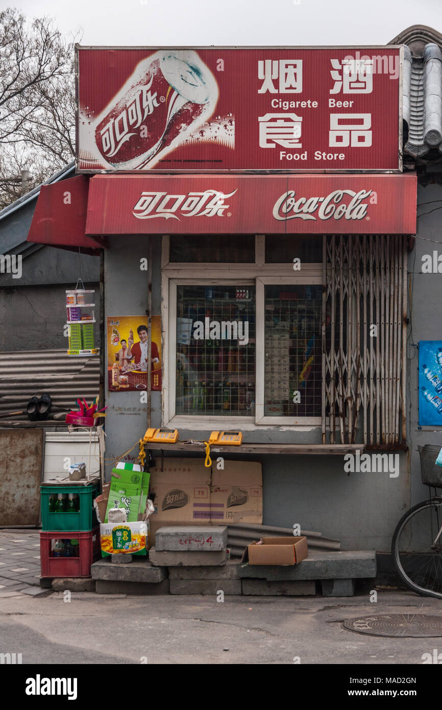 Peking, China - 26. April 2010: vordere Fenster kleiner Supermarkt mit roten Coca-Cola-Schild. Telefone, Kisten mit Flaschen und anderen Müll. Stockfoto