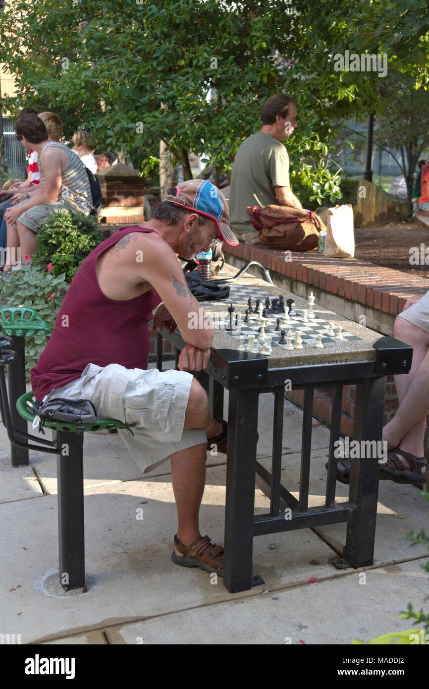 ASHEVILLE, NORTH CAROLINA - August 24, 2012: ein Mann Studien ein Schachbrett im Freien, während andere, die in der Innenstadt in Prichard Park im Sommer hängen Stockfoto