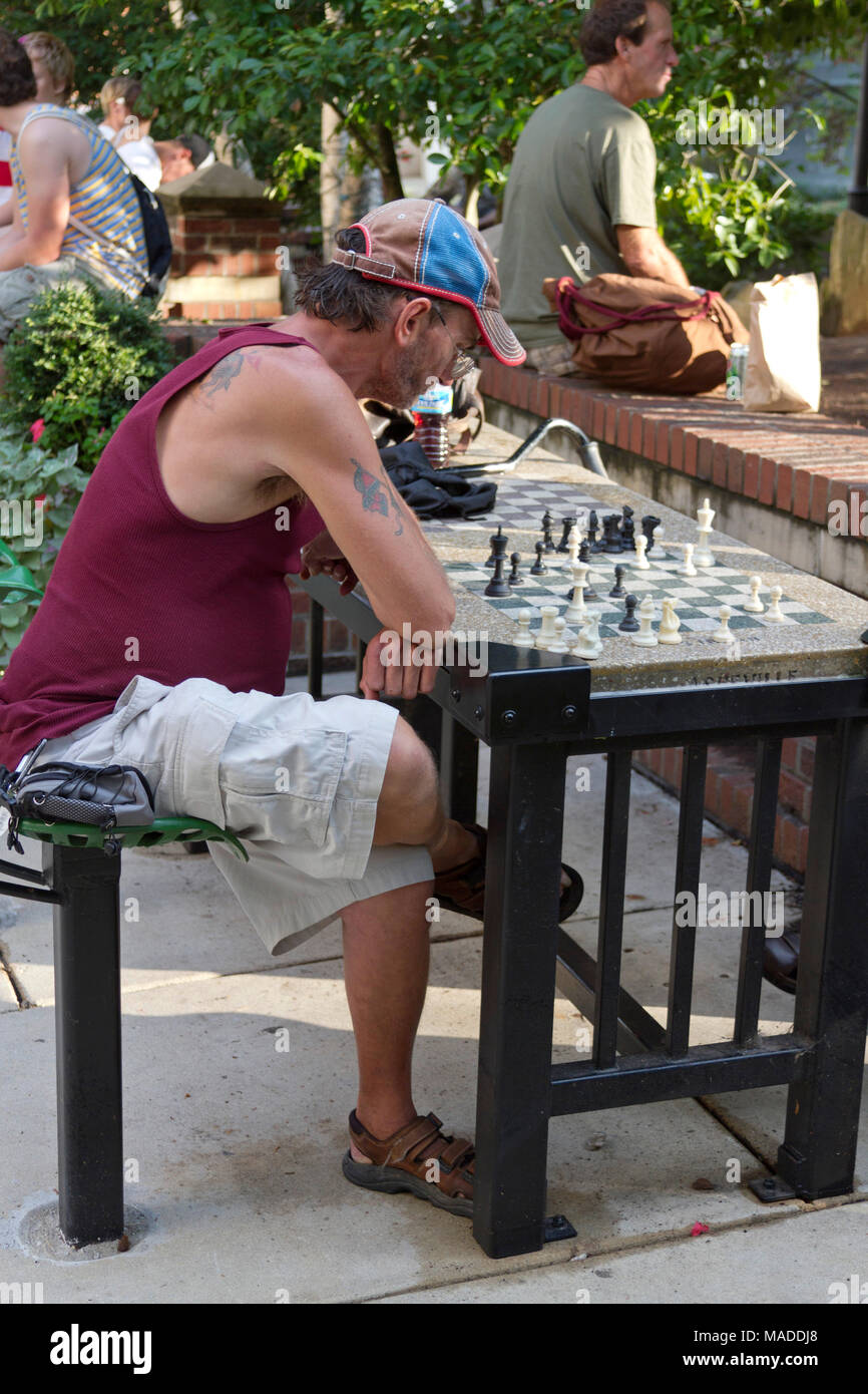 ASHEVILLE, NORTH CAROLINA - August 24, 2012: ein Mann Studien ein Schachbrett im Freien, während andere, die in der Innenstadt in Prichard Park im Sommer hängen Stockfoto